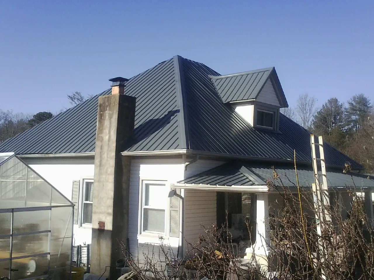 Dark blue standing seam metal roof on a white farmhouse with dormer — Slate & Tile Roof Repair by Roofing Brothers in Elba