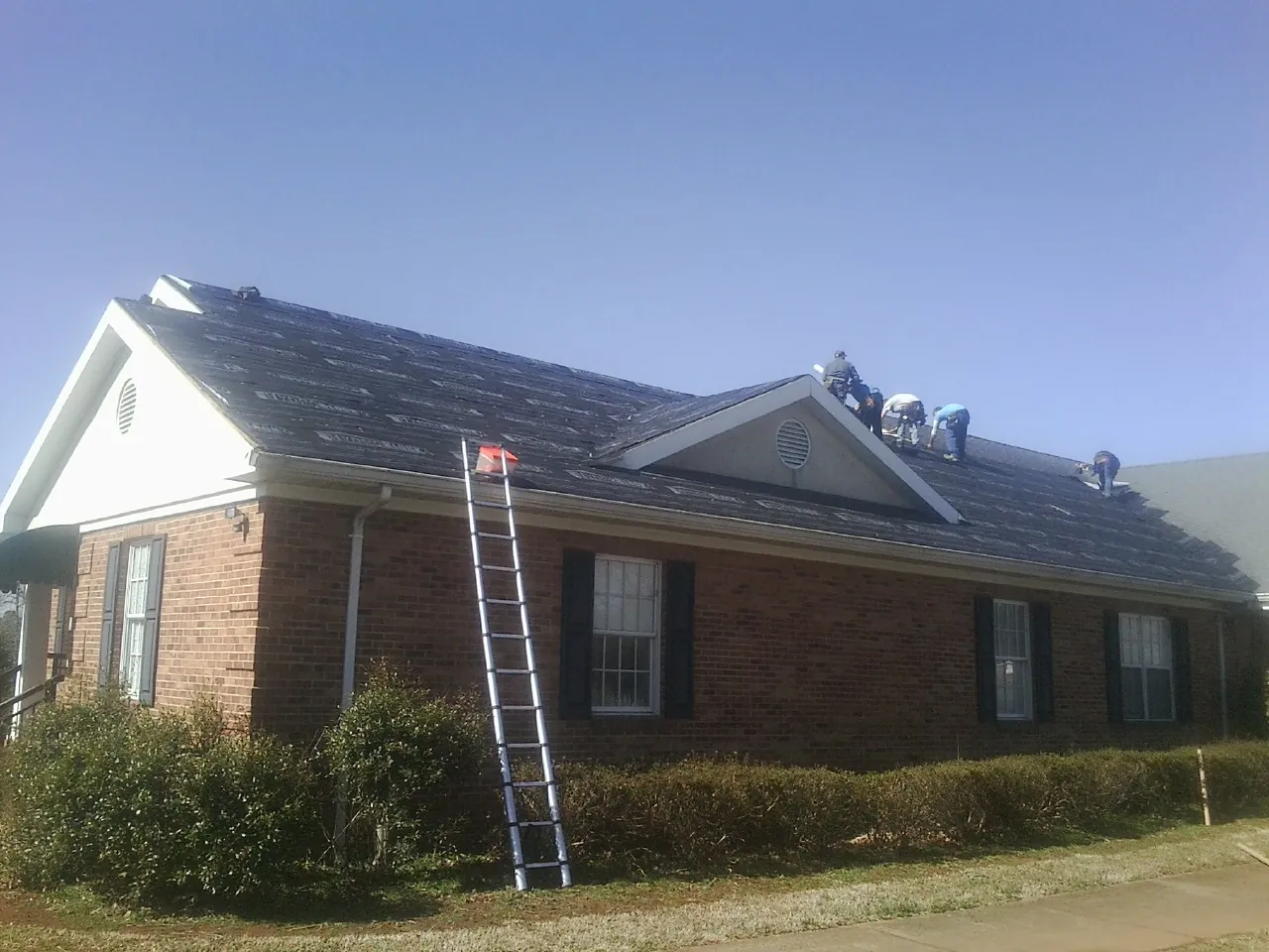 Crew tearing shingles off a brick ranch roof with a ladder set — Emergency Roof Repair work by our crew in Elba