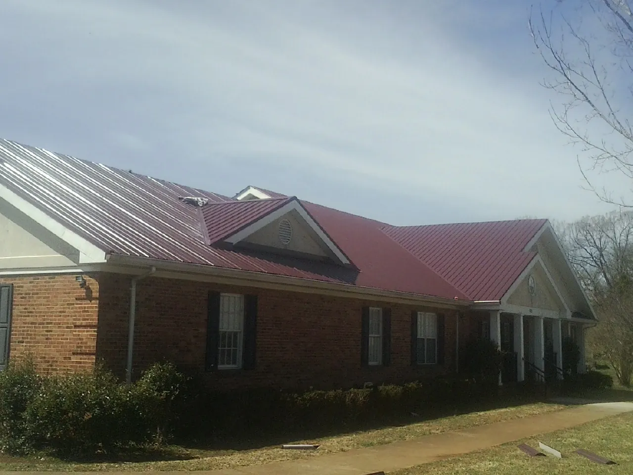 Red metal roof with gabled entries on a long brick building, from a Hail Damage Roof Repair job in Elba