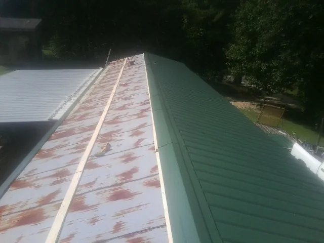 Old rusted panels beside newly installed green metal roofing — Wind Damage Roof Repair by Roofing Brothers in Elba