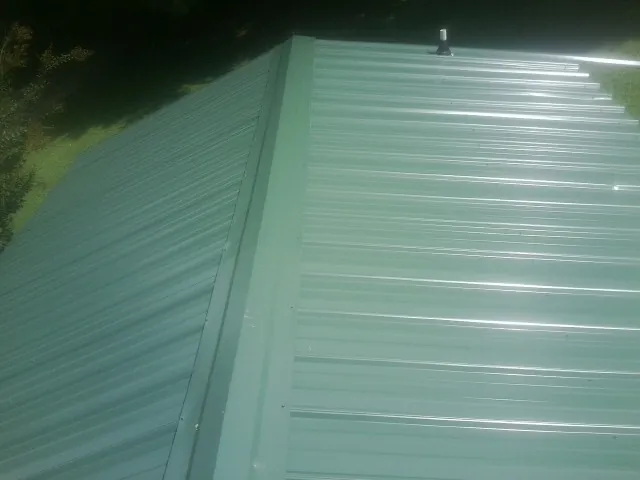 New green metal panels meeting at the ridge of a roof — Flat Roof Repair work by our crew in Elba