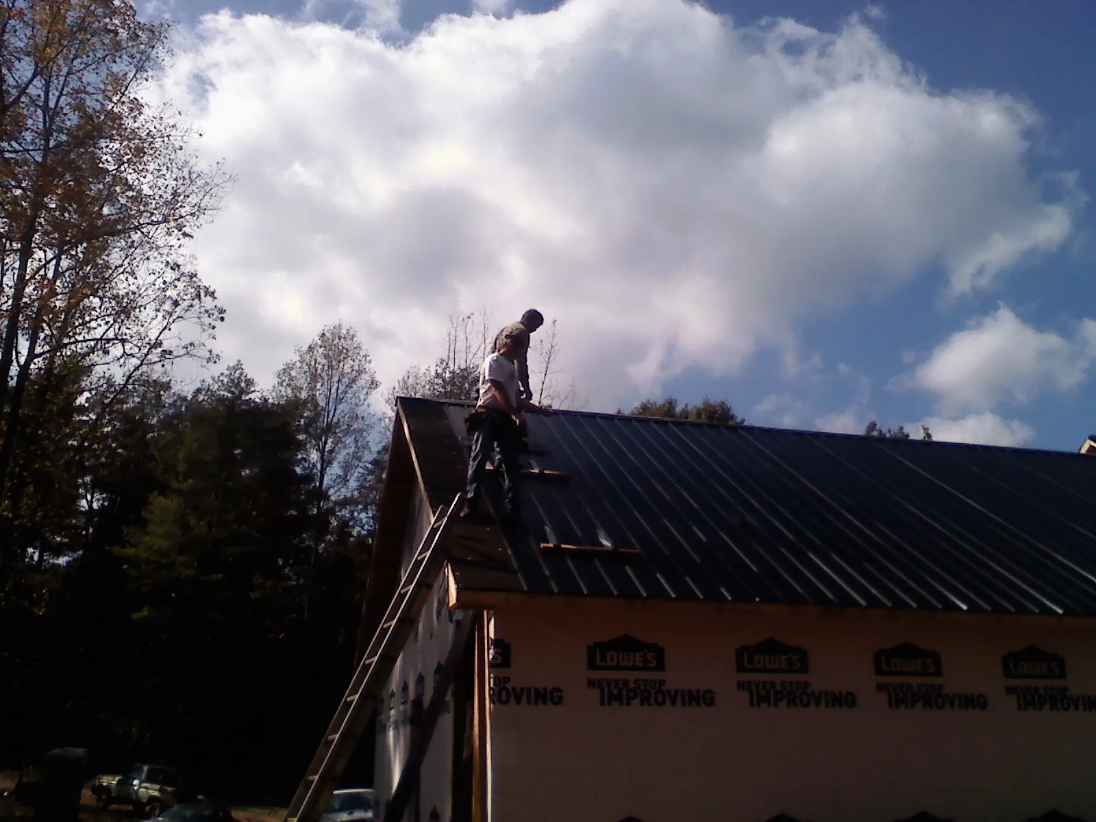 Roofer fastening dark metal panels high against a cloudy sky, from a Roof Inspection job in Elba
