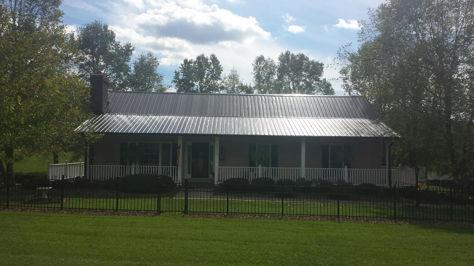 Gray metal roof on a brick ranch with a full width front porch — Gutter Guard Installation work by our crew in Elba