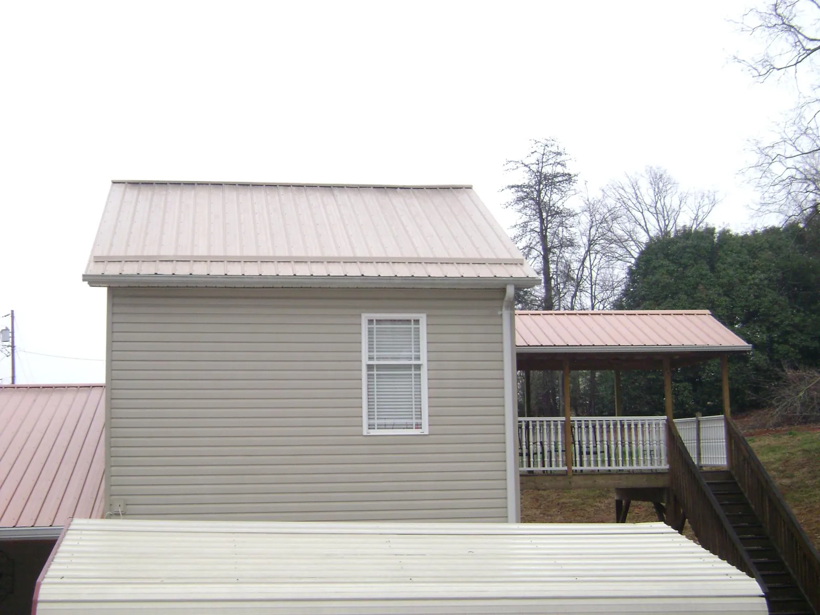 Tan metal roofs on a two story addition and attached porch, from a Roof Replacement job in Elba